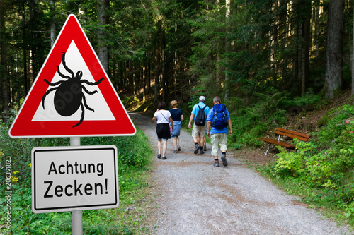 Schild mit Zeckenwarnung in Risikogebiet im Wald - mit Wanderern