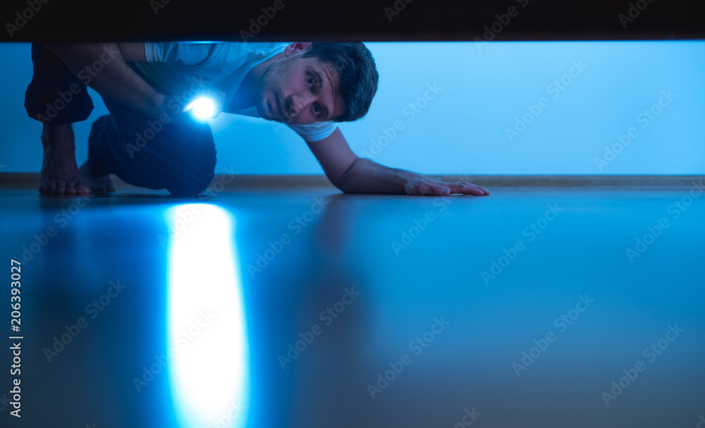 The man with a flashlight looking under the bed. evening night time - obrazy, fototapety, plakaty 