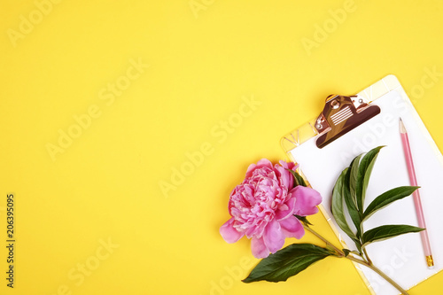 Top view of female worker desktop with clipboard, flowers and different office supplies items. Feminine creative design workspace.