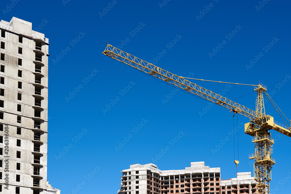 An urban building under construction with cranes against blue sky.