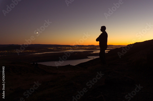A man on a mountain stands overlooking Reykjavik at night in Iceland