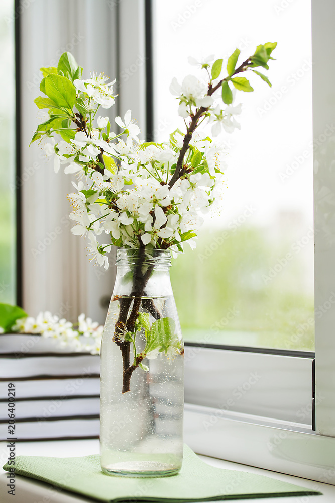 Naklejka premium bottle with branches of cherry blossoms on the window
