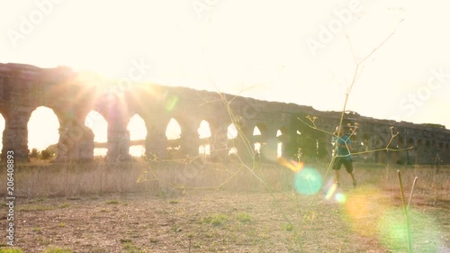 Young man in sportswear running along ancient roman aqueduct Appio Claudio. Training outdoor alone in peaceful park in Rome at sunset slow motion. photo