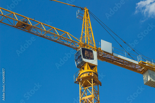 Yellow crane on blue sky background. Glass cabin of crane operator, boom, counterweight