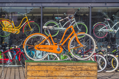 An orange bicycle on a wooden pedestal  in the background of a bicycle rental shop window