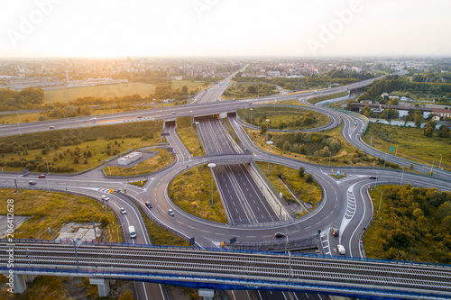 Aerial view of highway road junction at sunset. Highways, railway and green fields on the outskirts of the city. Transport concept.