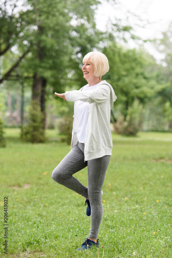 smiling elderly sportswoman exercising on green grass in park smiling elderly sportswoman exercising on green grass in park