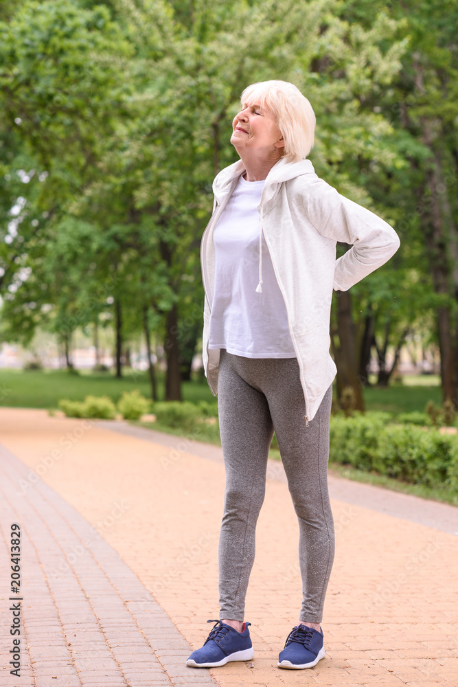 elderly sportswoman with back ache standing in park elderly sportswoman with back ache standing in park