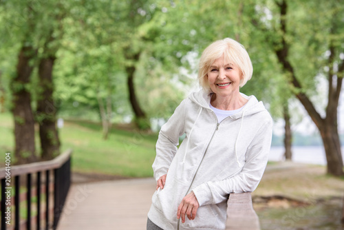 Фотография smiling senior woman standing near railings in park