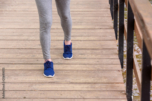 cropped view of sportswoman in sneakers walking on wooden path