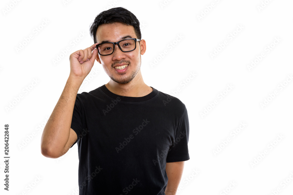 Studio shot of young happy Asian man smiling while holding eyegl Studio shot of young happy Asian man smiling while holding eyegl