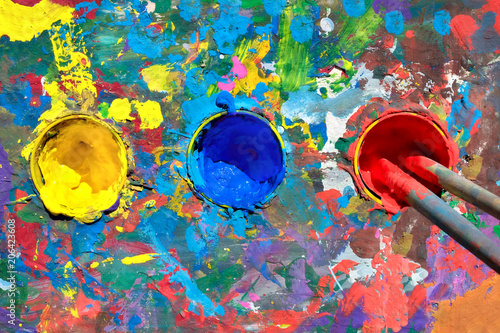 Gouache paint table with paint smears and cups with yellow, blue and red paints photo