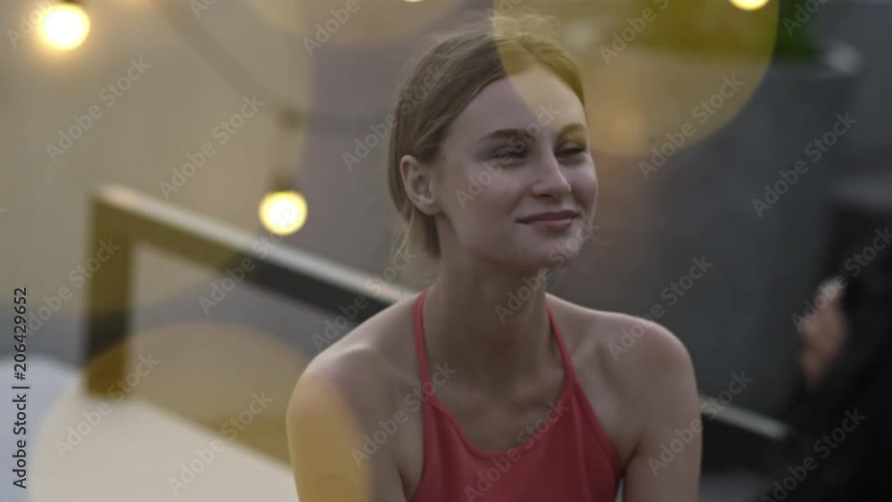Young woman sitting and relaxing after party, smiling and looking at her friend who comes and joins her Young woman sitting and relaxing after party, smiling and looking at her friend who comes and joins her