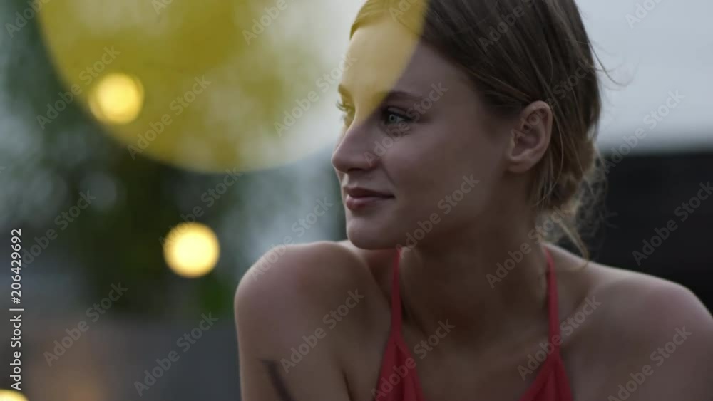 Medium shot of young pretty woman relaxing outdoors in the evening and listening to her friend