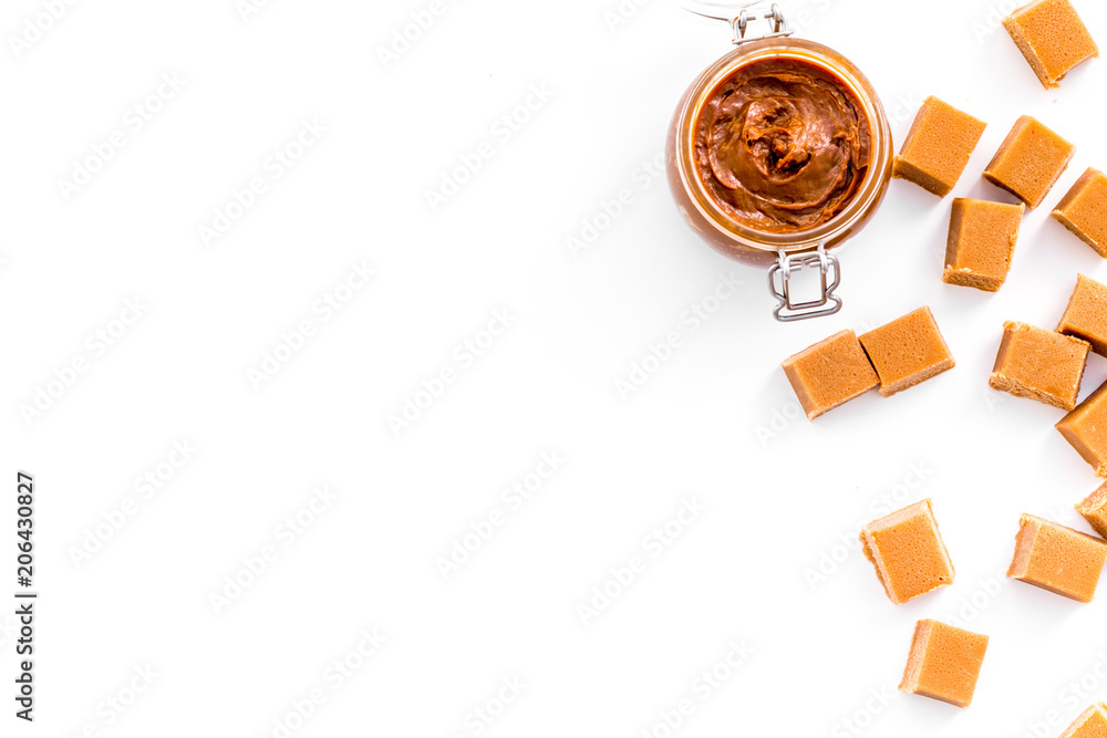 Caramel sauce in glass jar near caramel cubes on white background top view copy space Caramel sauce in glass jar near caramel cubes on white background top view copy space