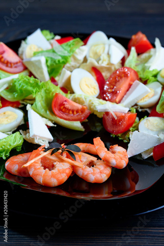 Mix salad with fresh vegetables and apetite shrimps in a black plate