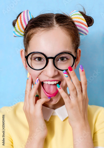 A young beautiful girl with a funny hairstyle wearing glasses is holding hands with a bright manicure near her face, laughing, rejoicing. A vivid image.