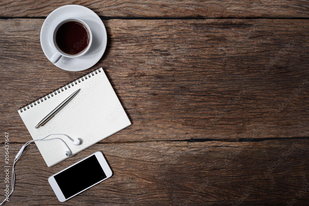 Office wooden desk with pen, notepad, coffee cup, smartphone and earphones. Top view Office wooden desk with pen, notepad, coffee cup, smartphone and earphones. Top view