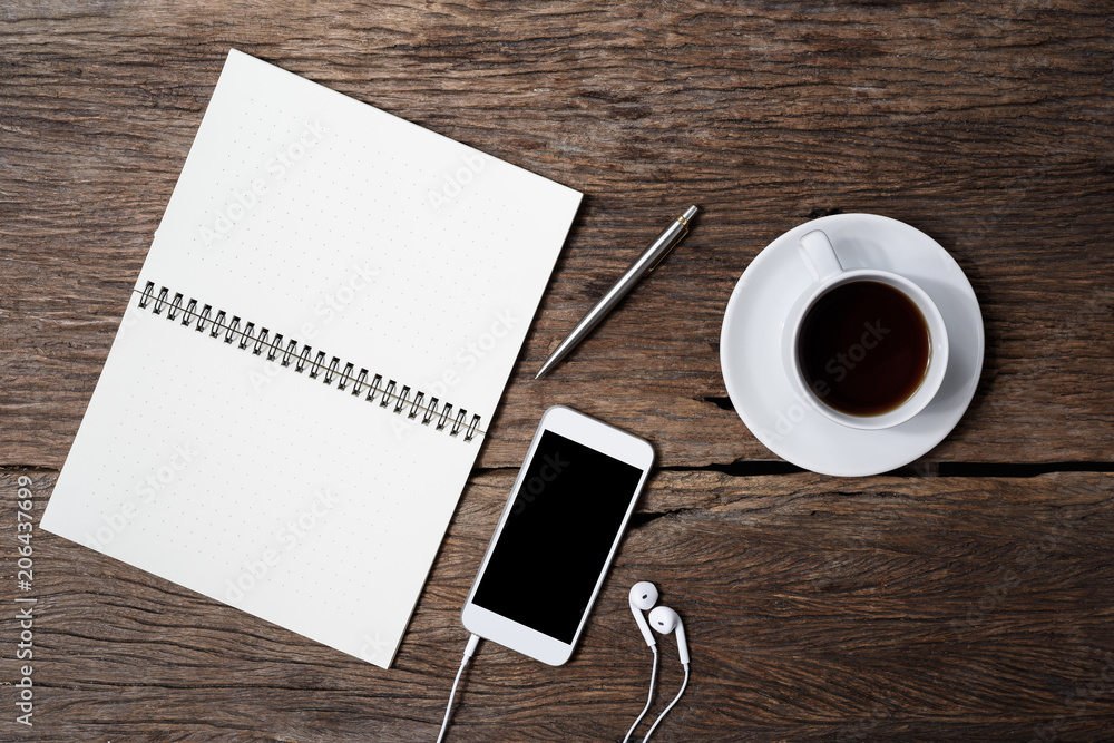 Office wooden desk with pen, notepad, coffee cup, smartphone and earphones. Top view Office wooden desk with pen, notepad, coffee cup, smartphone and earphones. Top view
