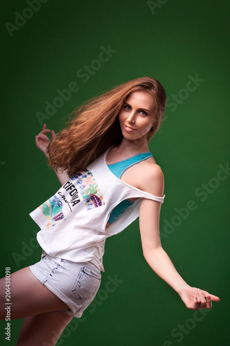Beautiful young blonde woman in white top in denim shorts smiling and posing on a black isolated background