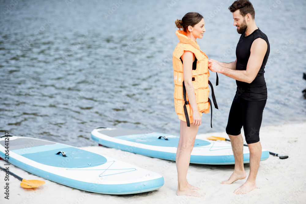 Obraz premium Male instructor helping to wear life vest on the woman preparing to surf on the standup paddleboard