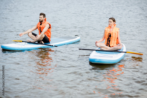 Couple in life vest relaxing on the stand up paddle board doing yoga © rh2010
