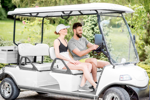 Young and happy couple having fun driving a golf cart during the summer sport activity