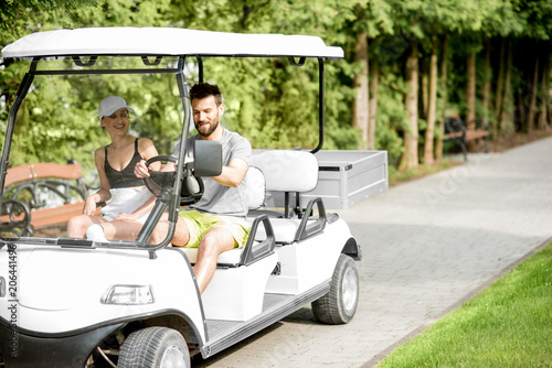 Young and happy couple having fun driving a golf cart during the summer sport activity