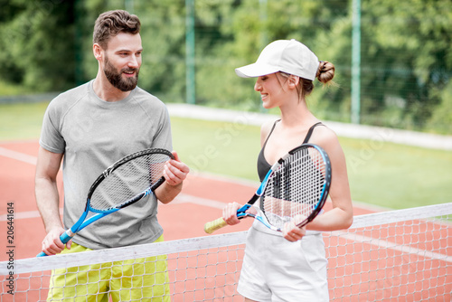 Young couple having fun standing together on the tennis court relaxing after the match outdoors