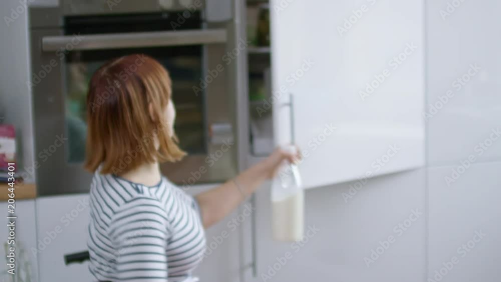 Handheld tracking of independent woman in wheelchair putting away milk bottle into fridge after finishing breakfast Handheld tracking of independent woman in wheelchair putting away milk bottle into fridge after finishing breakfast