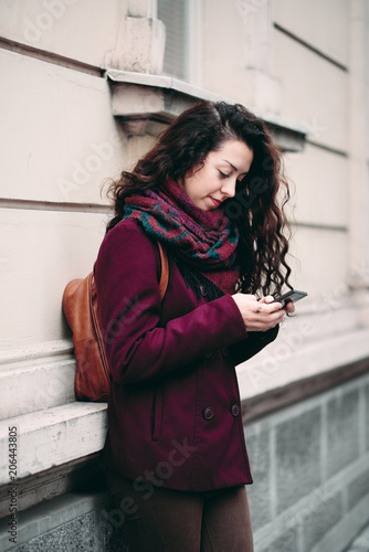 Girl standing against the wall on the street and using smart phone for texting. Free Download Girl standing against the wall on the street and using smart phone for texting. - GFXLoad