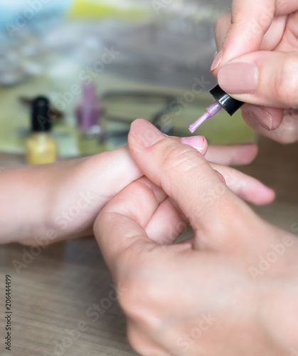 Mom paints daughter s nails on hands with pink nail polish on table
