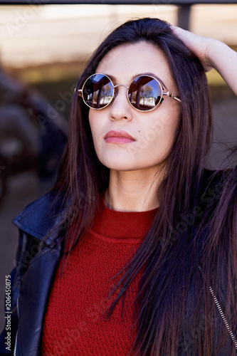 A large portrait of a young beautiful girl with glasses and a leather jacket. Urban style of the street. Cold season. Fashionable portrait. Sunglasses, glasses