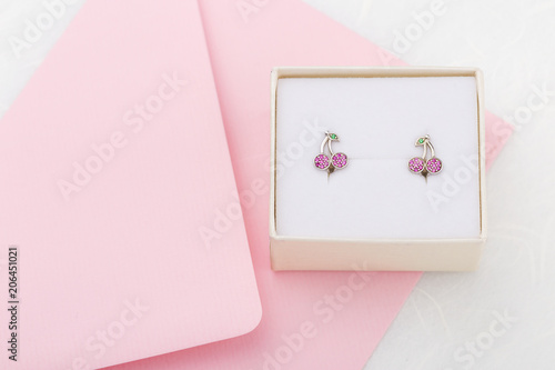 Cherry shaped earrings with crystals in gift box on pink envelope background with copy space