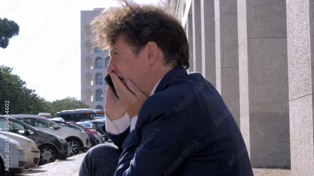Sad desperate business man starting to cry on the phone sitting on street Sad desperate business man starting to cry on the phone sitting on street