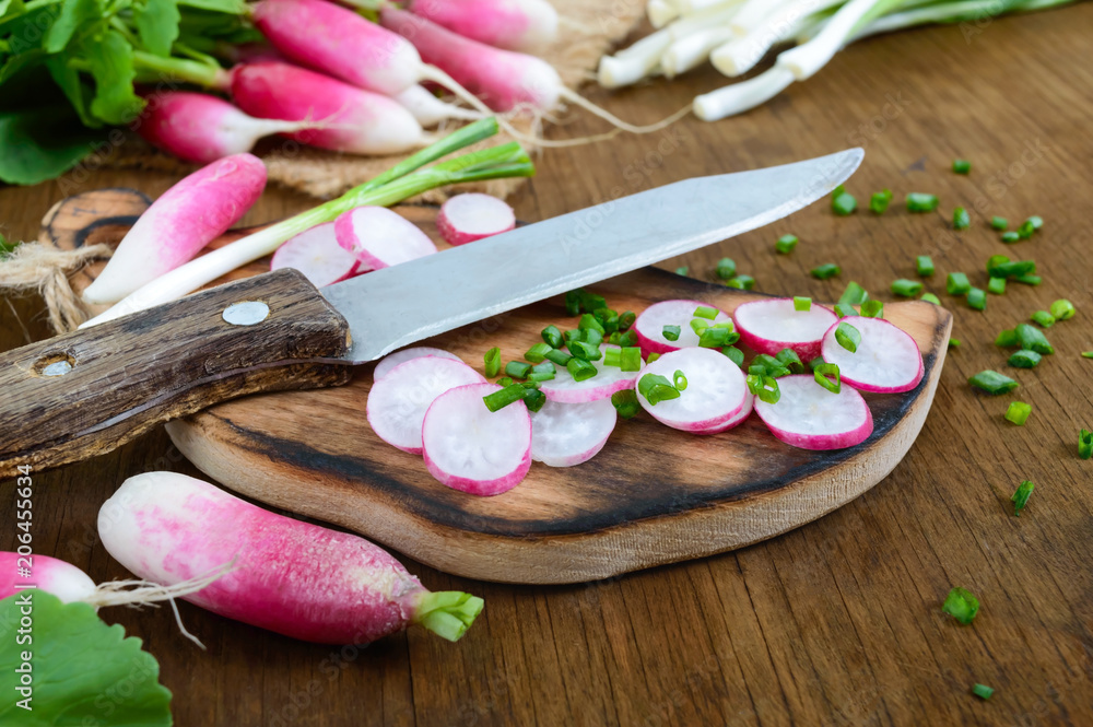 Sliced fresh red radishes and green young onions on white wooden background.  Healthy diet with radish. Ingredients for a light spring vegetable salad.