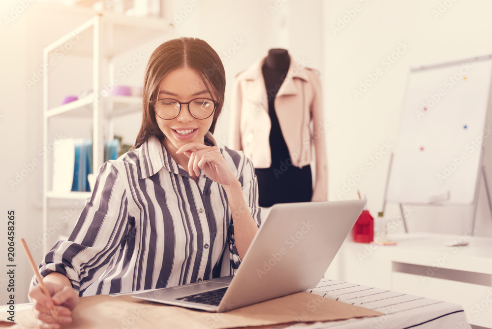 Endless enthusiasm. Close up of young concentrated designer sitting at the table while drawing clothing patterns and working with a laptop Endless enthusiasm. Close up of young concentrated designer sitting at the table while drawing clothing patterns and working with a laptop
