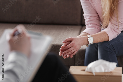 Close-up of woman's hands during counseling meeting with a professional therapist. Box of tissues and a hand of counselor blurred in the front. photo