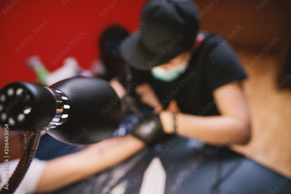 View from above of tattoo artist inking customers arm in his shop. View from above of tattoo artist inking customers arm in his shop.
