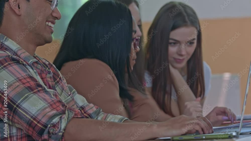 Command work in the university classroom with modern design and big spacy panoramic windows. Students coworking and helping each other, studying, learning, working with laptops and smartphones.