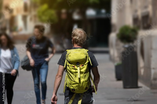 Man alone backpacker traveling round the world with his green backpack passing through the city