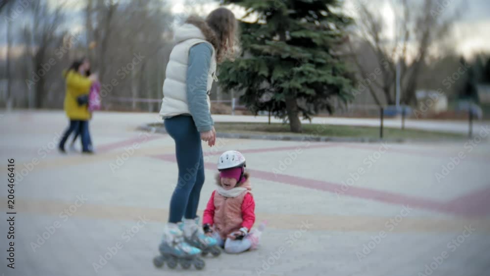 Mom and daughter ride on roller skates. Girl learning to roller skate, and falls. Mom teaches daughter to ride on rollers Mom and daughter ride on roller skates. Girl learning to roller skate, and falls. Mom teaches daughter to ride on rollers