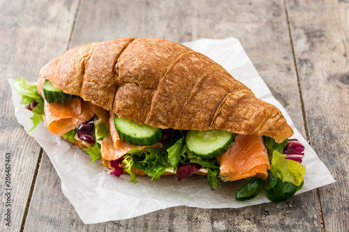 Croissant sandwich with salmon and vegetables on wooden table.