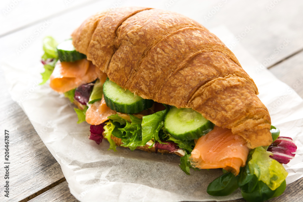 Croissant sandwich with salmon and vegetables on wooden table. Croissant sandwich with salmon and vegetables on wooden table.
