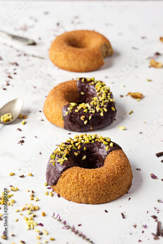 Ciambelle con glassa di cioccolato e granella di pistacchi su tavolo bianco in marmo photo