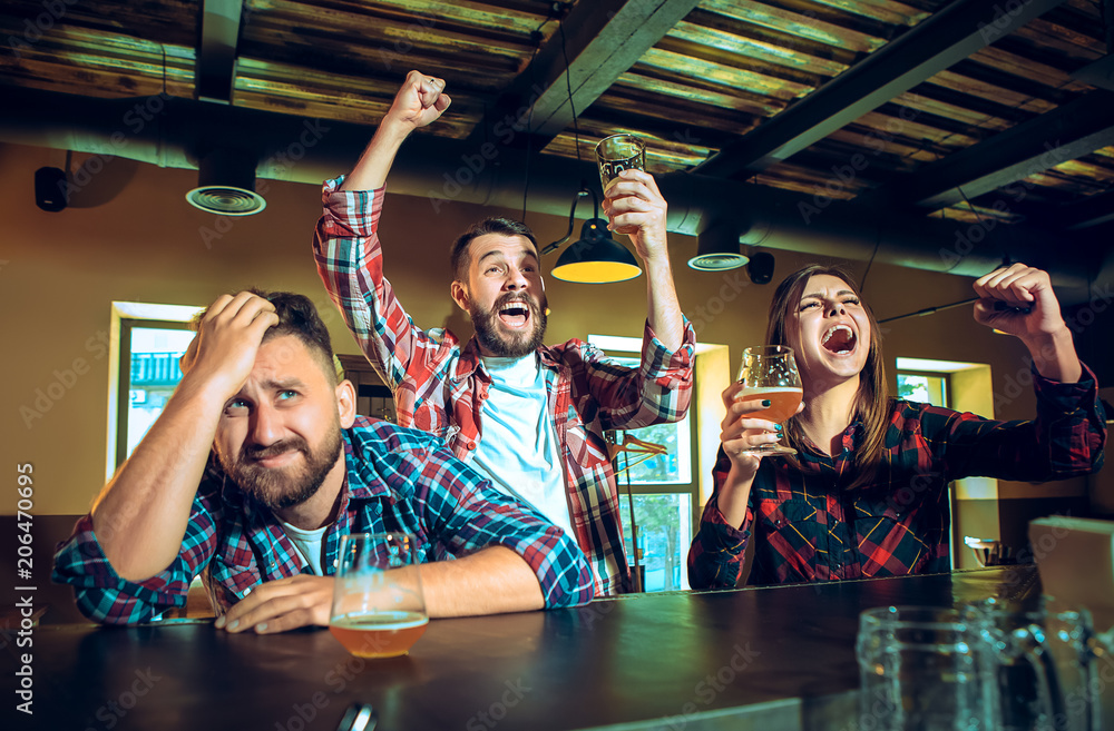 Fototapeta premium Sport, people, leisure, friendship and entertainment concept - happy football fans or male friends drinking beer and celebrating victory at bar or pub