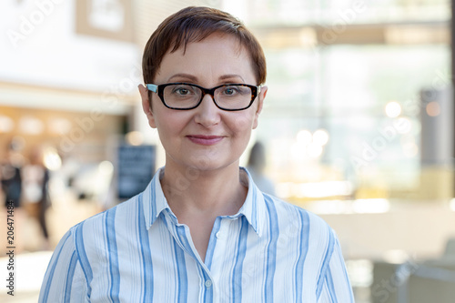 Closeup portrait of middle aged woman wearing glasses. Professional headshot of businesswoman, teacher, manager. Blurred office background.