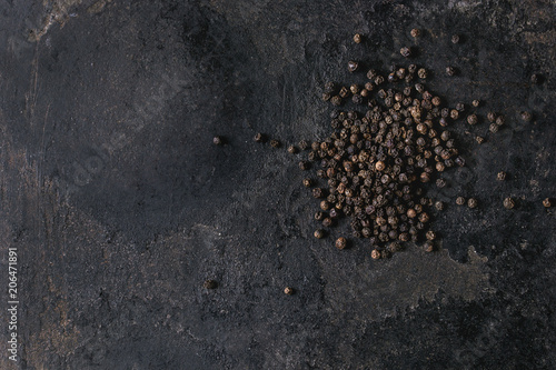 Heap of black pepper peppercorns over old black iron texture background. Top view, copy space.