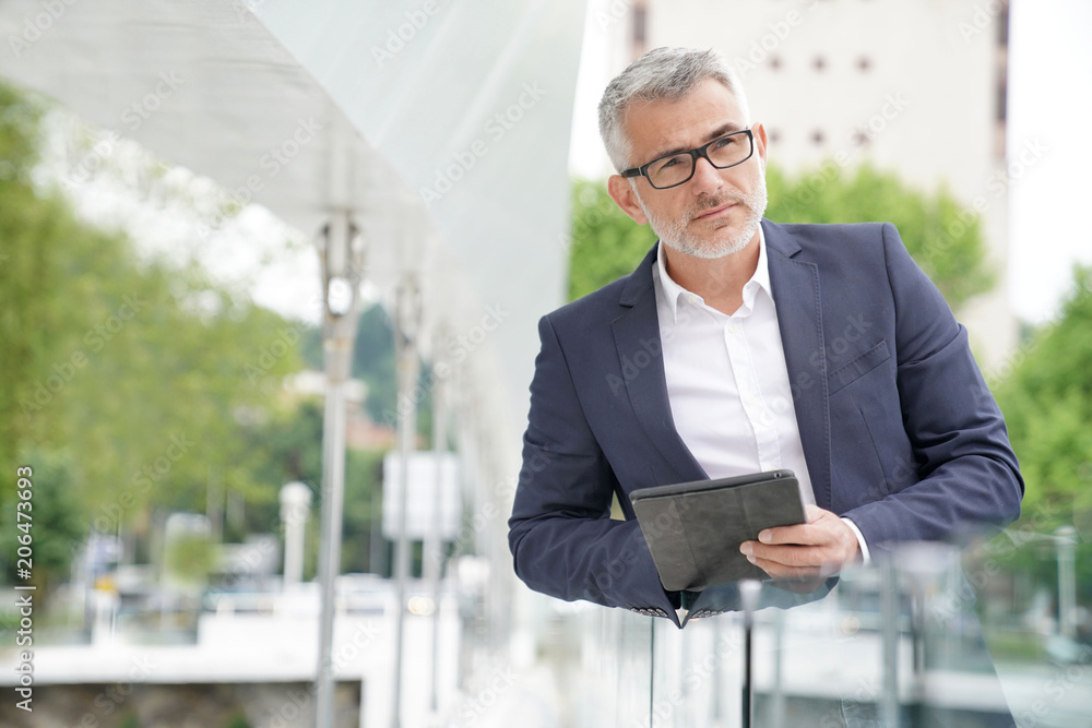Fototapeta premium Businessman in city street connected with digital tablet