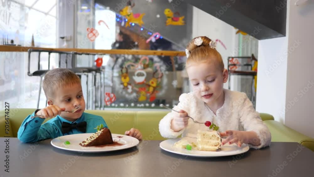 Cute kids in cafe, boy and girl eating sweet pieces of cake with a fork Cute kids in cafe, boy and girl eating sweet pieces of cake with a fork